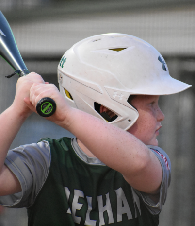 A young boy in a Pelham baseball shirt stands at home plate ready to bat.